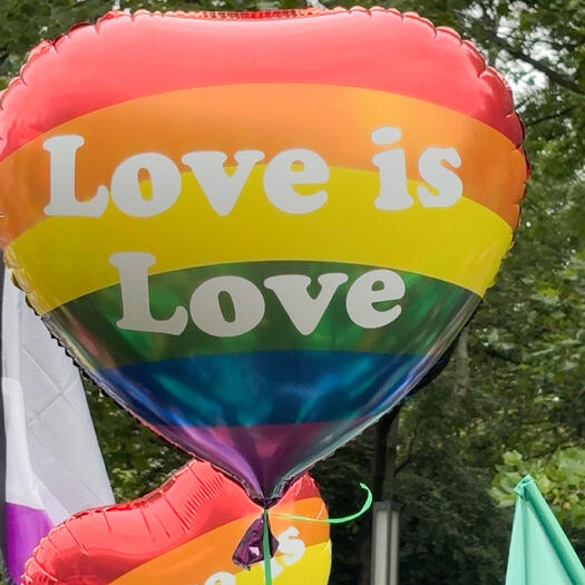 Ein Luftballon in Farben vom Regenbogen. Er hat die Form eines Herzen. Darauf steht Love is Love. Das heißt auf Deutsch: Liebe ist Liebe