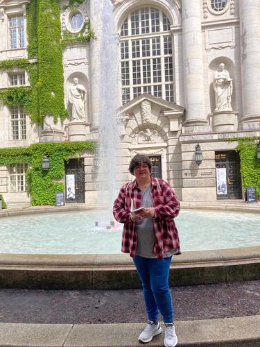 Katzenauge steht mit einem Buch vor einem Springbrunnen der Staatsbibliothek