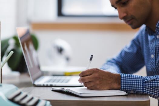 Ein Mann sitzt am Laptop und schreibt in ein Heft. Foto: Stocksnap auf Pixabay