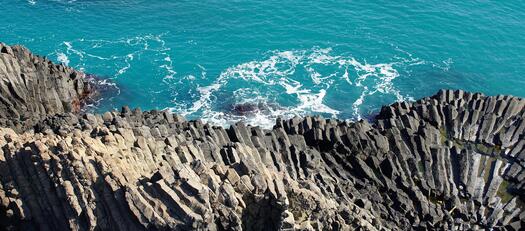 Ein steiler Felsen und das blaue Meer.