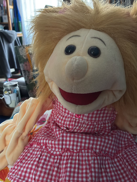 Eine Bauchredner-Puppe: Sie hat blonde Haare und trägt ein rotweiß-kariertes Kleid.