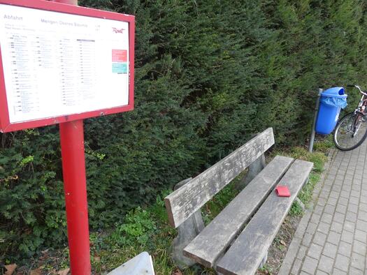 An der Bushaltestelle steht eine Bank. Darauf liegt eine rote Brieftasche.