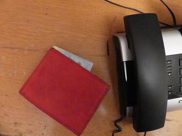 Auf einem Tisch liegt eine rote Brieftasche. Ein Geldschein schaut heraus. Daneben ist ein schwarzes Telefon.