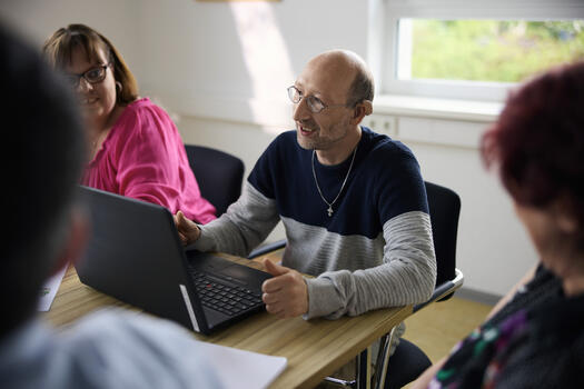 Menschen mit Beeinträchtigung sitzen an einem Tisch. Sie arbeiten mit einem Laptop. Foto: David Mauer, Lebenshilfe