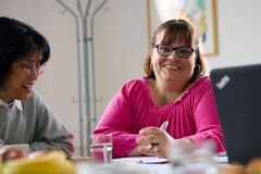 Lächelnde Frau blickt in die Kamera; neben ihr sitzt eine andere Frau (Foto: Lebenshilfe/David Maurer)