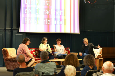 Vier Menschen sitzen bei der Preisverleihung auf einer Bühne und sprechen zum Publikum.