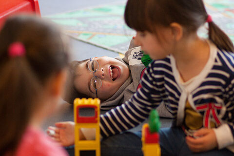 Blick durch zwei spielende Mädchen auf am Boden liegenden, lachenden Jungen (Foto: Sybille Baier)